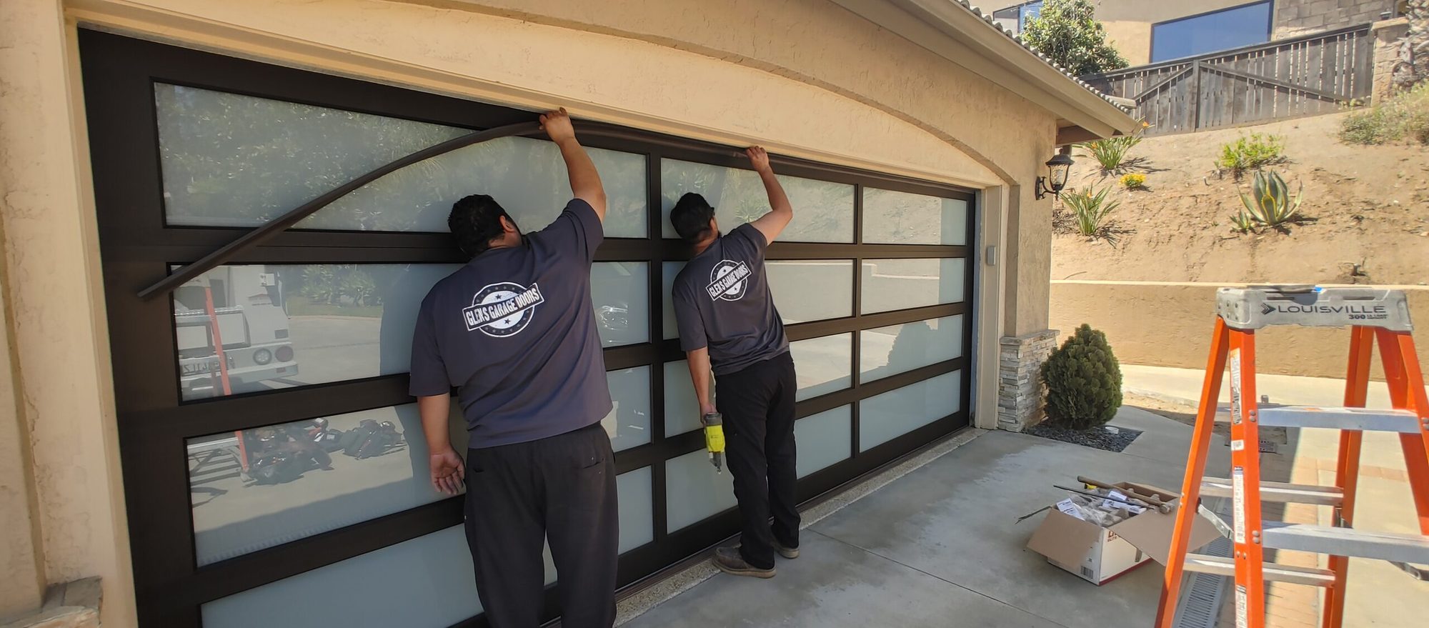 Two Glen's technicians installing a full-view aluminum and glass garage door from outside